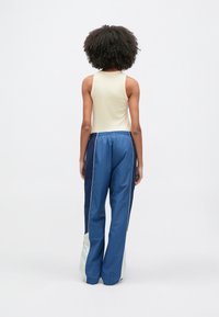 Ανοιχτό μπεζ αμάνικη μπλούζα συνδυασμένη με μπλε παντελόνι φόρμας που διαθέτει αντίθετες πλαϊνές πινελιές και ρυθμιζόμενο κορδόνι στη μέση, με απαλή υφή.