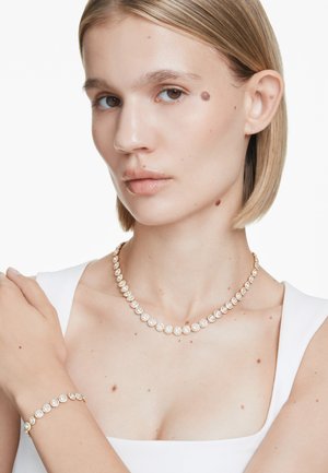Gouden halsketting en armband met ronde zettingen met duidelijke, sprankelende edelstenen. Gladde, gepolijste afwerking met een klassiek ontwerp.