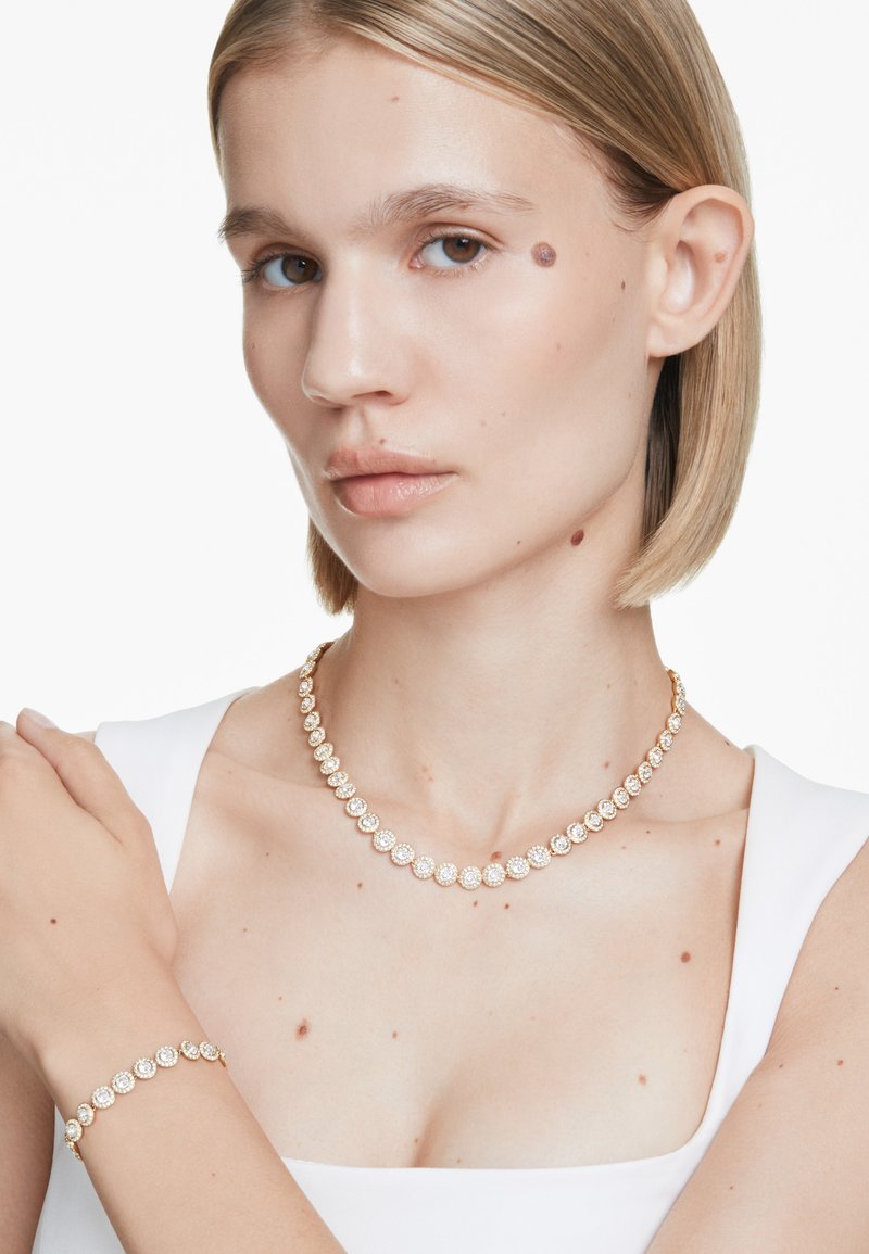 Goldfarbene Halskette und Armband mit runden Einstellungen und klaren, funkelnden Edelsteinen. Glatte, polierte Oberfläche mit klassischem Design.