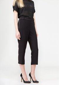 Černé kalhoty s vysokým pasem, zúženým střihem a zkrácenými nohavicemi, v kombinaci s průhledným černým pruhovaným topem a černými lodičkami na vysokém podpatku.