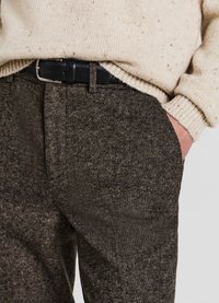 Braune, strukturierte Wollhose kombiniert mit einem cremefarbenen Pullover und einem schwarzen Gürtel. Auffällige Details sind sichtbare Nähte und Taschen.