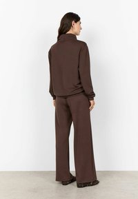 Brown two-piece loungewear set featuring a high-collar, long-sleeve top and wide-leg pants, made of soft, textured fabric.