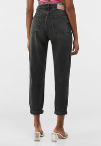 Tmavě šedé džíny s vysokým pasem a ohrnutými nohavicemi, které mají dvě zadní kapsy a decentní texturovanou látku. V kombinaci s sandály na průhledném podpatku.