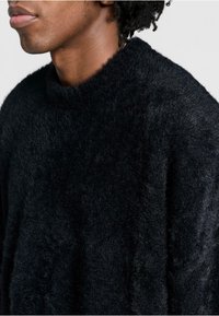 Schwarzer flauschiger Pullover mit hohem Kragen und weicher Textur; hat eine lockere Passform und keine sichtbaren Muster oder Hardware-Details.