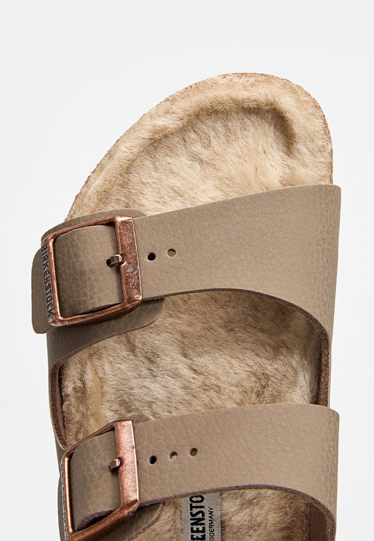 Sandale en cuir marron avec deux sangles ajustables et boucles en cuivre, doublure en fausse fourrure beige douce et semelle de contournement.