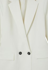 Blazer bianco con rever a punta, doppio bottone nero, tasche laterali, forma strutturata e texture del tessuto liscia.