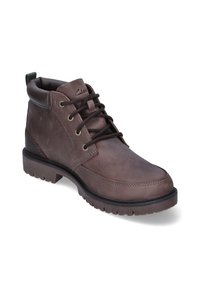Bota de cuero marrón con cordones, cuello acolchado, ojales de metal, suela gruesa y lengüeta en el talón, inclinada para mostrar el lado exterior.