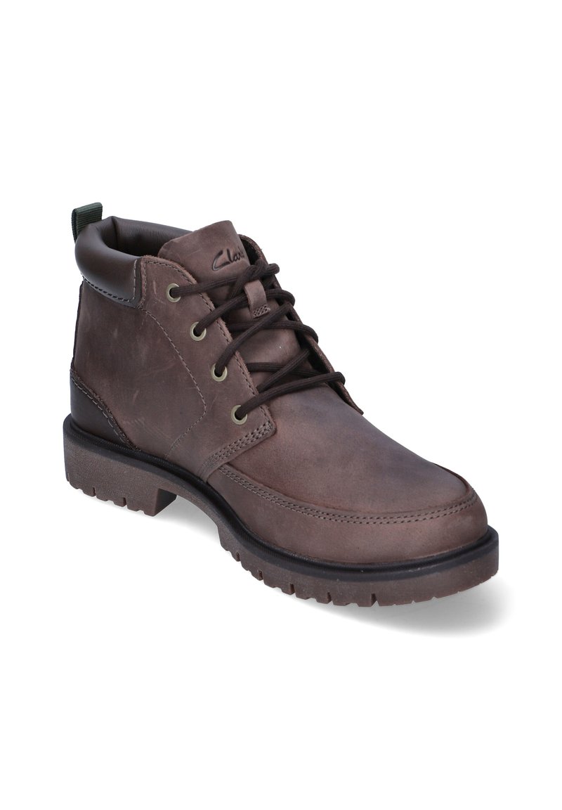 Botte en cuir marron à lacets avec col rembourré, œillets en métal, semelle épaisse et languette au talon, anglée pour montrer le côté extérieur.