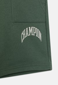 Pantalones cortos de algodón verdes que presentan un logo curvado de "CHAMPION" en blanco en la parte frontal, con una textura suave y costuras en el dobladillo estándar.