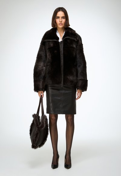 Veste en fausse fourrure noire avec fermeture éclair à l'avant, manches larges et col montant, associée à une jupe crayon en cuir noir et un sac à main assorti.