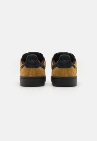 Suede sneakers with a brown upper, black accents, and rubber soles. Features a padded collar and subtle branding on the heel.