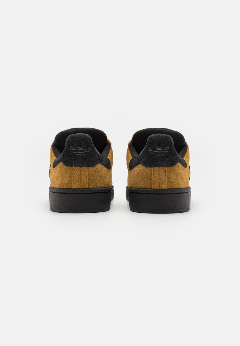 Zapatillas de ante con parte superior marrón, acentos negros y suelas de goma. Cuentan con un collar acolchado y un sutil branding en el talón.