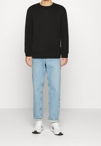 Felpa nera con maniche lunghe, collo rotondo e polsini a costine, abbinata a jeans dritti blu chiaro e sneakers bianche sportive.