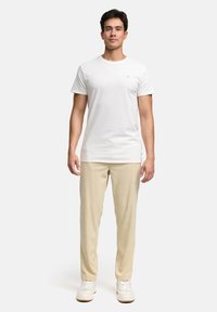 White crew-neck t-shirt paired with light beige textured pants and white sneakers, standing against a neutral background.
