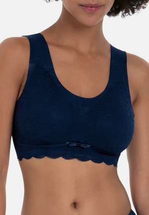 Vrouw draagt een marineblauwe kanten bralette met brede bandjes en een klein strikje aan de voorkant, getoond van schouders tot taille.
