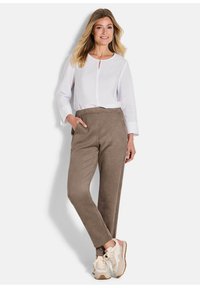 Lichtgewicht witte blouse met een keyhole halslijn, gecombineerd met gladde, taupe tapered broeken. Het model draagt beige sneakers met roze accenten.