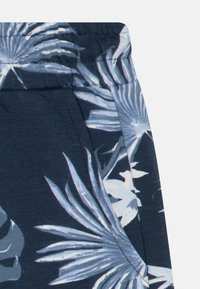 Marineblauwe stof met witte en lichtblauwe tropische bladerenpatronen en zichtbare naden aan de zijkant en de tailleband.