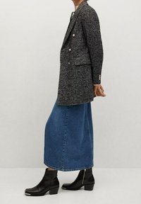 Blazer a righe bianche e nere, doppiopetto, slim fit. Indossato con una lunga gonna in denim blu e stivali neri alla caviglia con punta quadrata.