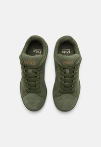 Gröna mockaskor med rund tå, platt gummisula och texturerade skosnören. "Polo"-logotyp på en ljusbrun lapp nära tungan.