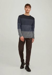 Heren trui met lange mouwen in grijze verloopkleuren, met een ronde hals en een gebreide textuur, gecombineerd met donkere broek en zwarte laarzen.