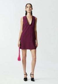Abito senza maniche a scollo a V in tessuto bordeaux con scollatura decorata di perline, abbinato a una borsa rosa e tacchi in vernice nera.