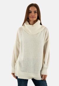 Witte, oversized trui met een hoge, opgevouwen kraag. Zachte, textuurstof, lange mouwen en een rechte zoom. Gecoord met donkere jeans.