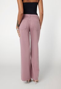 Džínsy so širokými nohavicami v jemnej ružovej džínsovine, s stredne zvýšeným pásom, zadnými vreckami s šikmými klapkami a surovým okrajom. Hladký predný diel s jemným povrchom.