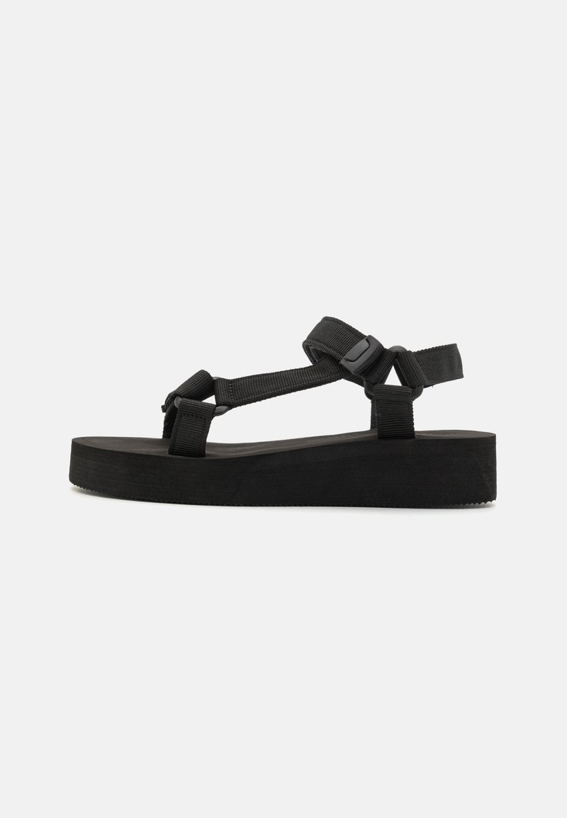 Black platform sandals featuring a thick foam sole, fabric straps, and adjustable buckles for secure fit. Smooth texture and minimal design.