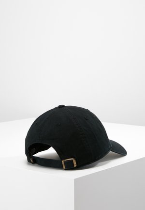 Black adjustable baseball cap with metal buckle closure, viewed from the back, resting on a white surface.