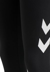 Czarne legginsy sportowe wykonane z elastycznego materiału, z wyraźnym białym wzorem chevron po boku dla dodatkowego efektu wizualnego.