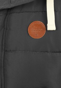 Gepolsterte graue Jacke mit strukturiertem Stoff, einem runden braunen Lederpatch mit der Aufschrift "BLEND" und einem cremefarbenen Kordelzug.