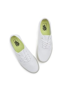 Witte canvas sneakers met een gladde textuur, ronde neus, vetersluiting en een groene binnenzool met een zwart logo.