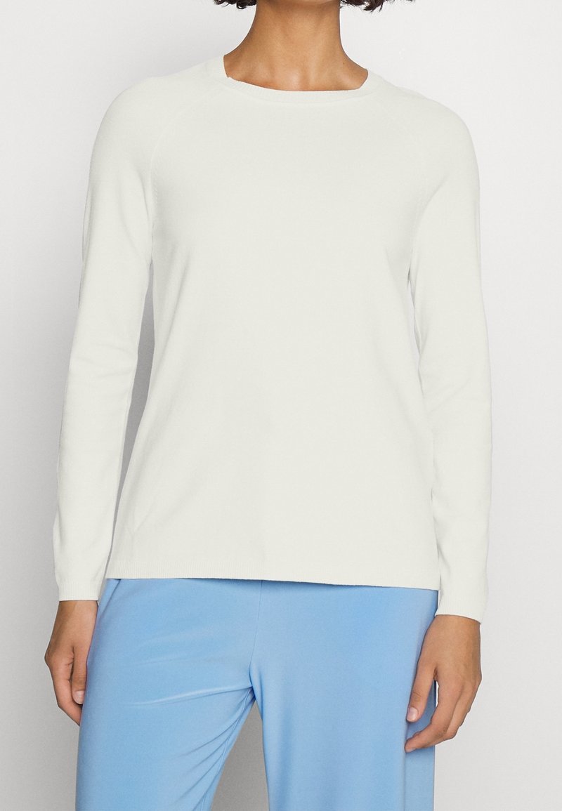 Vit långärmad topp med rund halsringning, ribbade muddar och en slät yta, i kombination med ljusblå byxor.