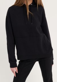 Sudadera negra con capucha, bolsillo delantero, ajuste holgado, mangas largas y cordón ajustable. Material suave y puños acanalados.