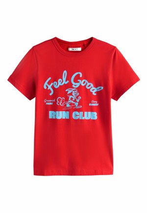 Raudona medvilninė trumpomis rankovėmis ir apvalia iškirpte marškinėliai. Ant jų yra mėlynos spalvos grafika su užrašu „Feel Good RUN CLUB“ ir bėgančio triušio iliustracija.