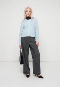 Jasnoniebieski dziergany kardigan na guziki, zestawiony z szarymi szerokimi spodniami z wysokim stanem oraz czarnymi szpilkami z noskiem w szpic. W komplecie czarna torebka.