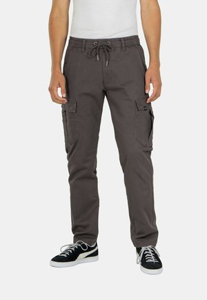 Pantalones cargo grises con cintura elástica y cordón, que cuentan con bolsillos laterales y un diseño de pierna ajustada. Combinados con zapatillas negras.