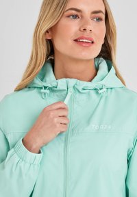 Lightweight mint-green jacket with a front zipper, adjustable hood, and elastic cuffs. Features embroidered "TOG24" logo on chest.