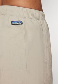 Beige shorts with an elastic waistband, featuring a patch pocket and a black Patagonia logo tag near the waist. Texture appears lightweight.
