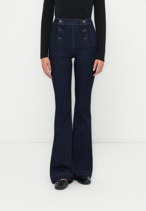 Høyt livdark denim flared bukser med knappet front, to sidelommer og frynset hem. Materialet ser mykt ut med en lett glans.