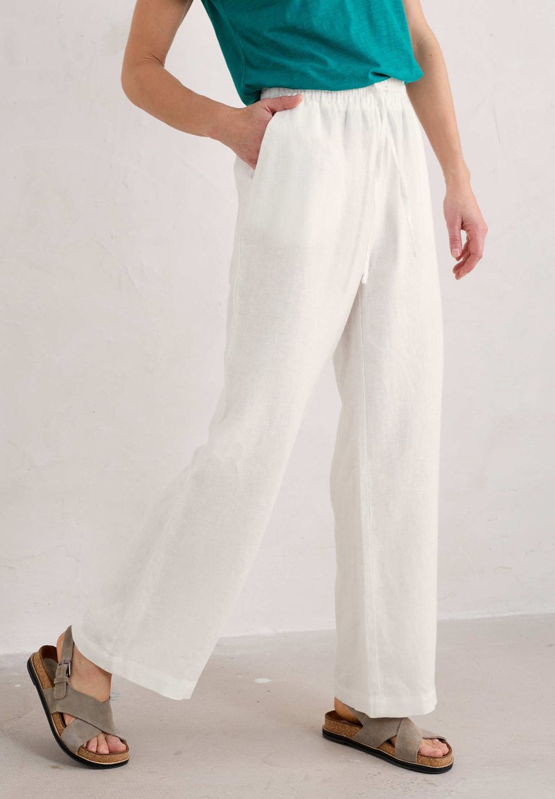 Witte linnen brede broek met een elastische tailleband en zijzakken, gecombineerd met grijze sandalen met bandjes en een kurken zool.