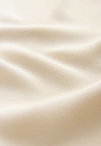 Tissu beige doux avec une surface lisse, légèrement texturée et des plis délicats créant des ombres et des reflets subtils.