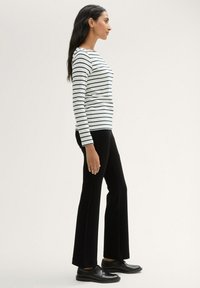 White long-sleeve top with navy stripes, paired with black flared trousers and black lace-up shoes, viewed from the side.