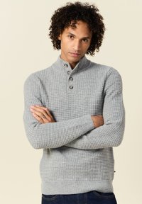 Suéter gris de punto con cuello alto, tapeta de tres botones, tejido texturizado y puños y dobladillo acanalados.