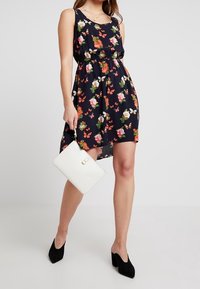 Černé květinové šaty se sítí na těle, zdobené vícenybarevnými květinami a motýly. Doplněné bílou kabelkou a černými vysokými podpatky.