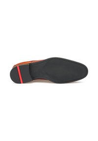 Suole di scarpe da cerimonia in pelle nera con una striscia rossa vicino al tallone, che mostrano una fine cucitura e la marchiatura del brand su uno sfondo bianco.