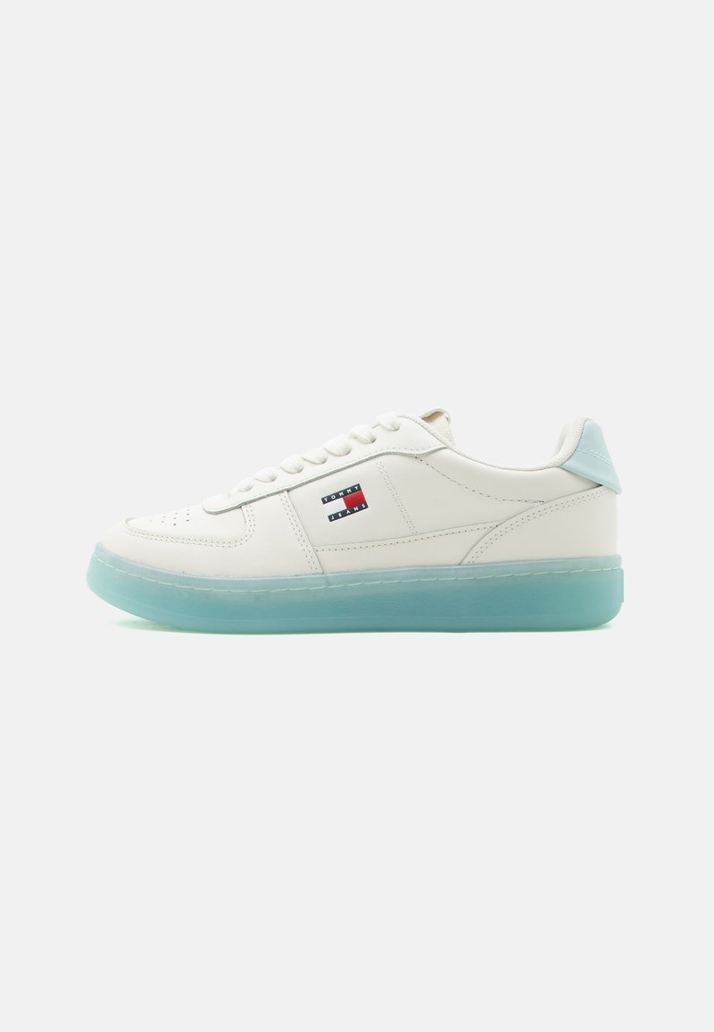 Baskets basses blanches avec semelle translucide bleu clair et logo Tommy Jeans sur le côté, présentées de profil sur un fond blanc.