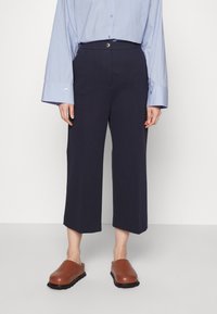 Marinblå korta byxor i slät tyg, med en framknäppning, sidofickor och en avslappnad passform, matchade med bruna träskor.