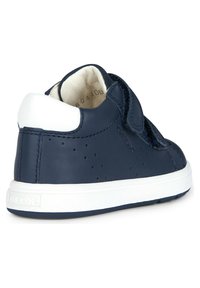 Chaussure en cuir bleu marine avec un capuchon de talon blanc, une sangle Velcro, des côtés perforés et une semelle en caoutchouc blanc. Design simple et arrondi.