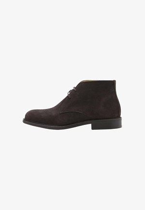 Stivaletti alla caviglia in suede marrone scuro con una texture liscia, punta arrotondata, due asole per i lacci e un tacco in gomma basso e piatto.